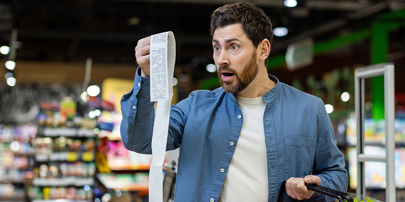 Man looking at supermarket receipt with a shocked look on his face