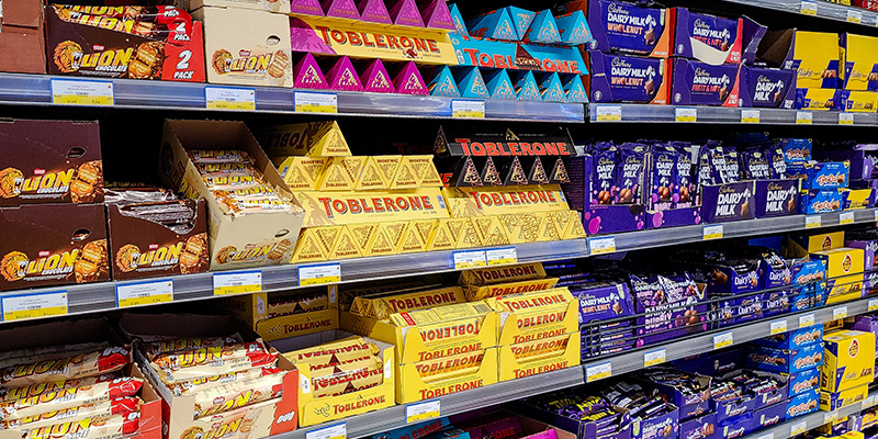 Supermarket shelves display a range of choclates including toblerone, dairy milk, twirl and more